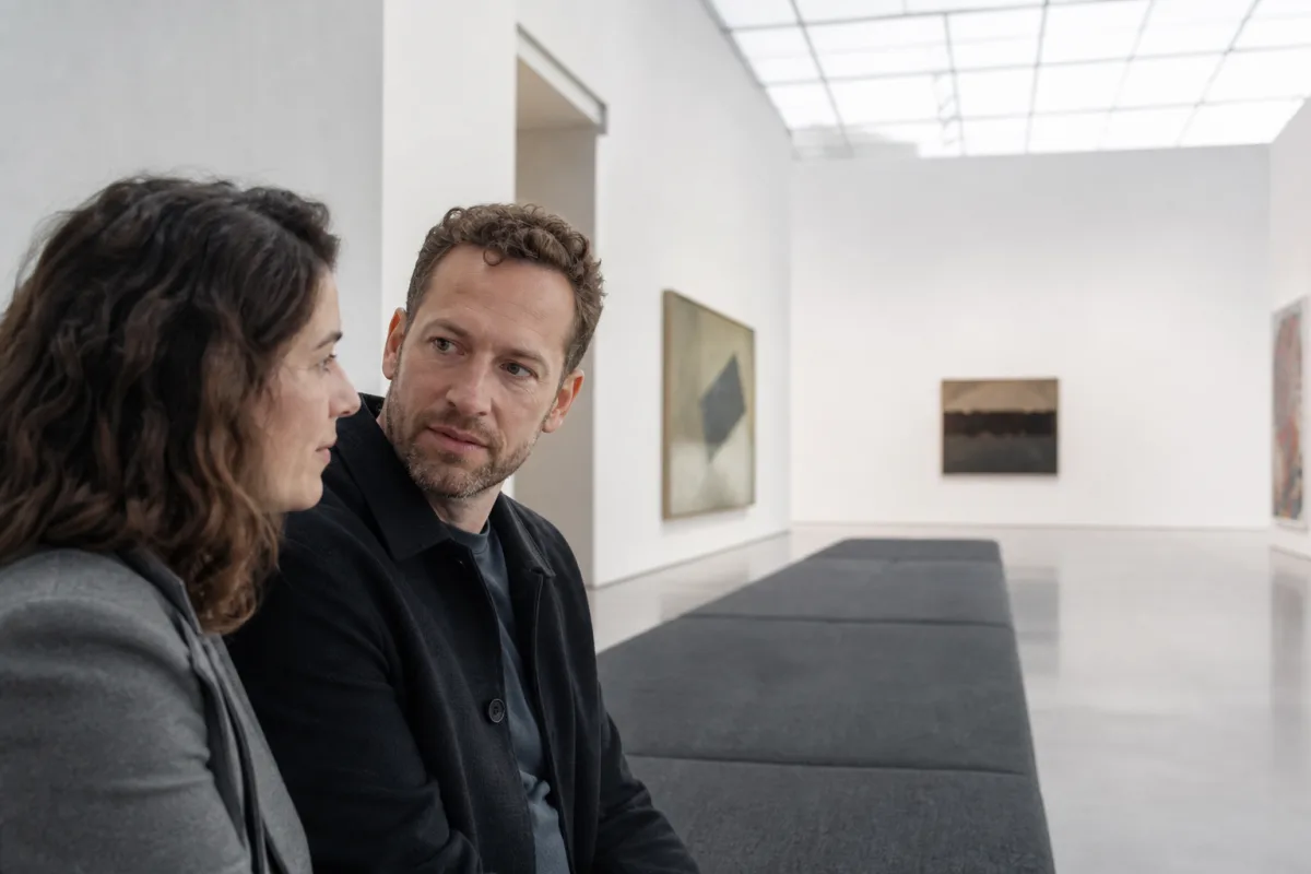 An ambiamorous adult couple sitting together on a gallery bench with open space for other partners